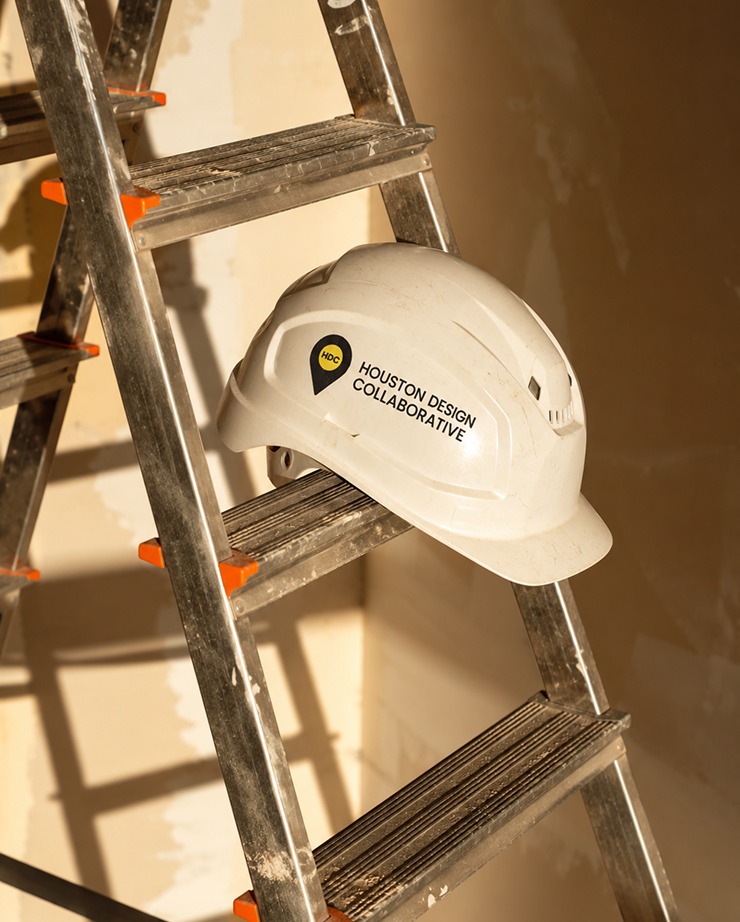 A Houston Design Collaborative branded hard hat resting on a ladder.