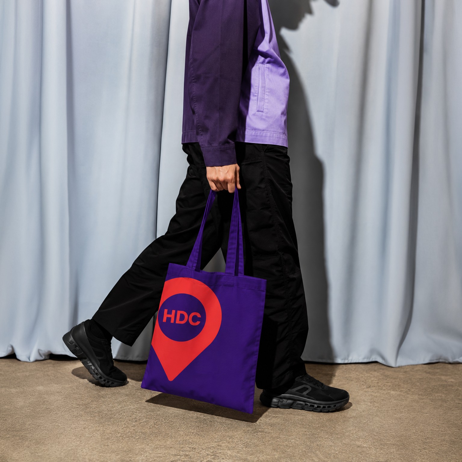 A person walking while carrying a purple Houston Design Collaborative tote bag.
