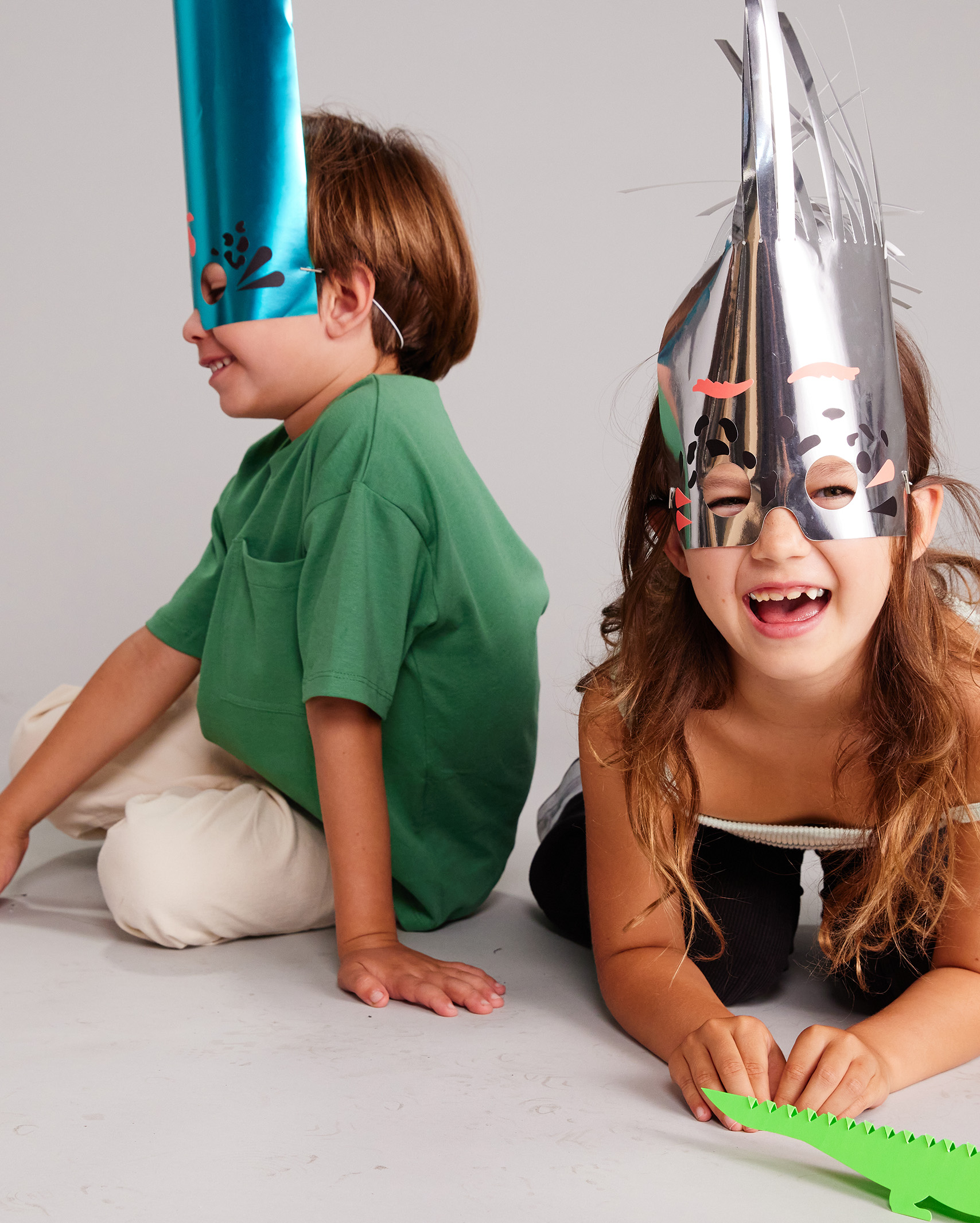 Two kids wearing foil party hats, laughing.